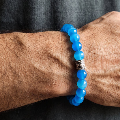 Blue agate bead bracelet on arm with dark engraved metal centerpiece near cuff.