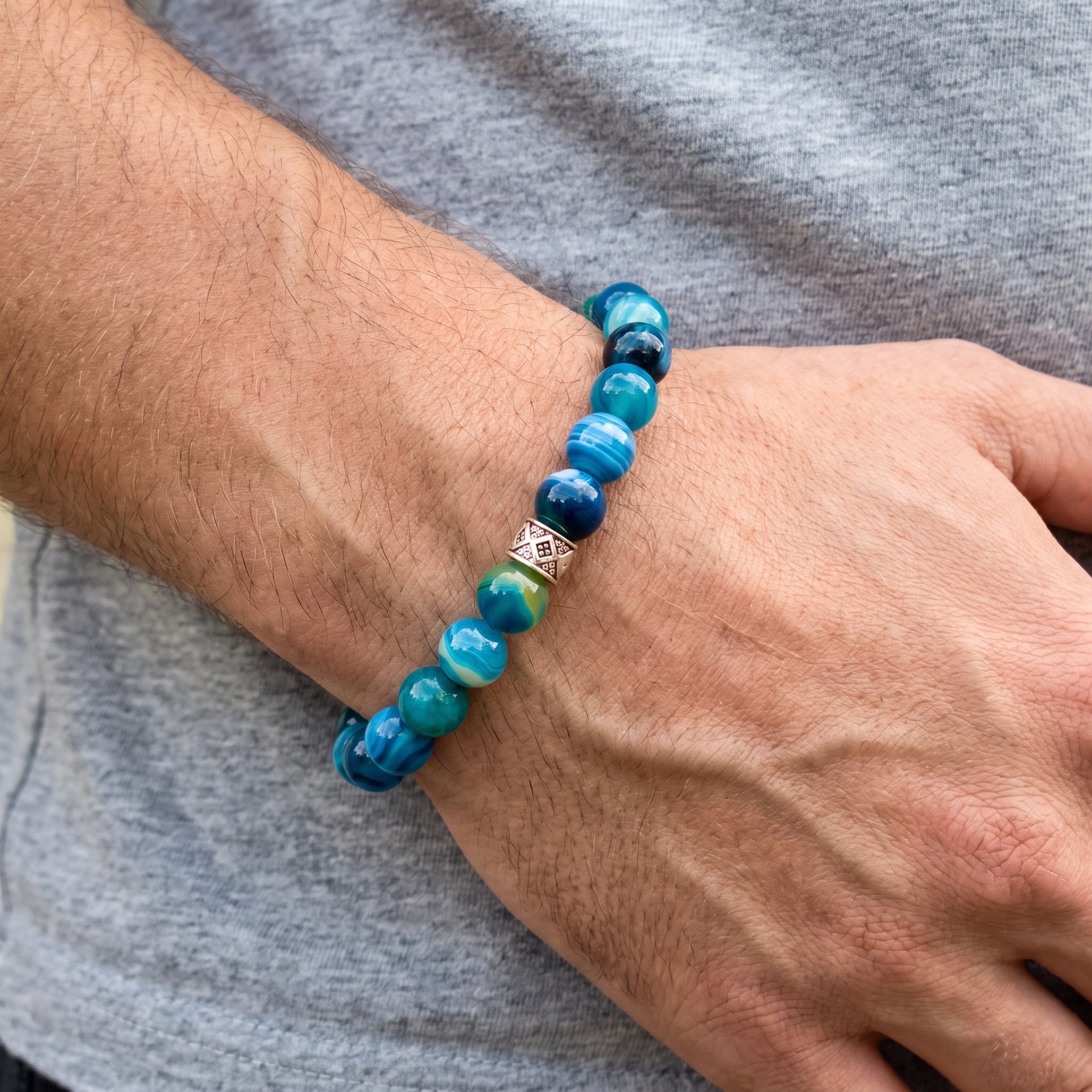 Agate bead bracelet on a man’s wrist: blue and teal beads with silver diamond centerpiece