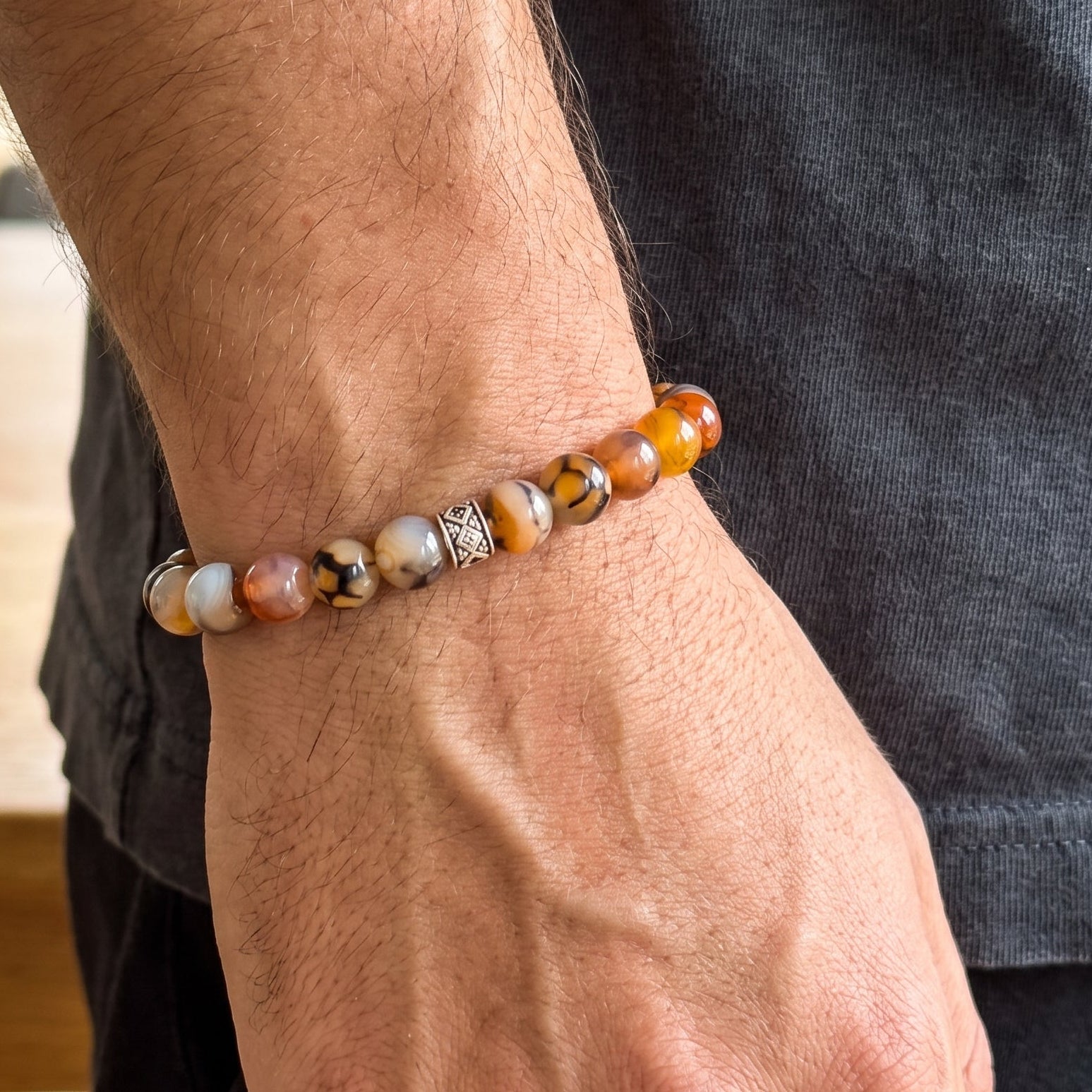Agate beaded bracelet on wrist with orange-brown and white stones and a silver geometric centerpiece