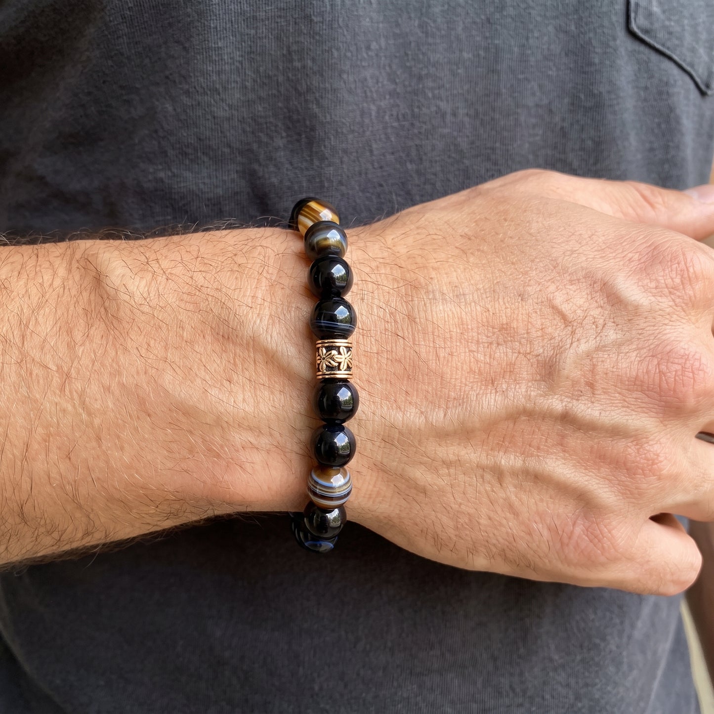 Men's agate bracelet worn on wrist, dark round beads with gold-tone caps