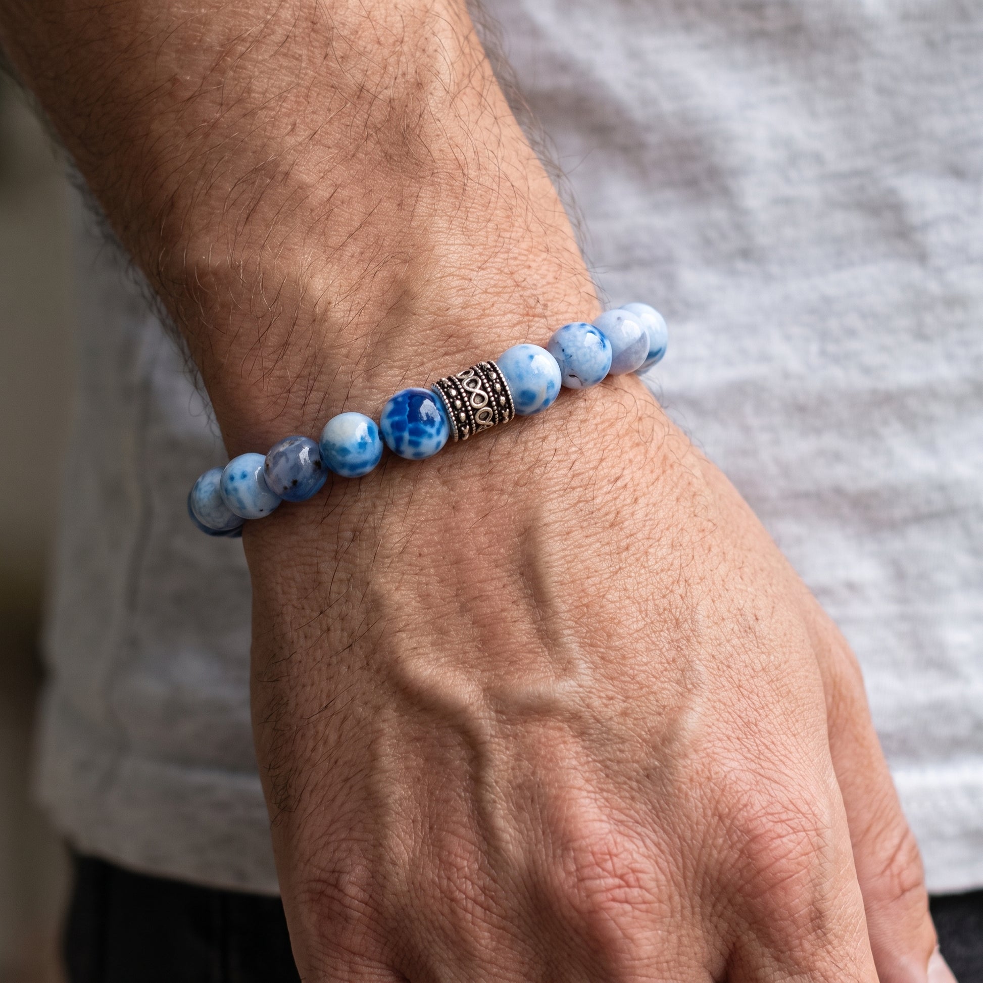 Agate bead bracelet on a man’s wrist in blue and white beads with a black metal spacer.