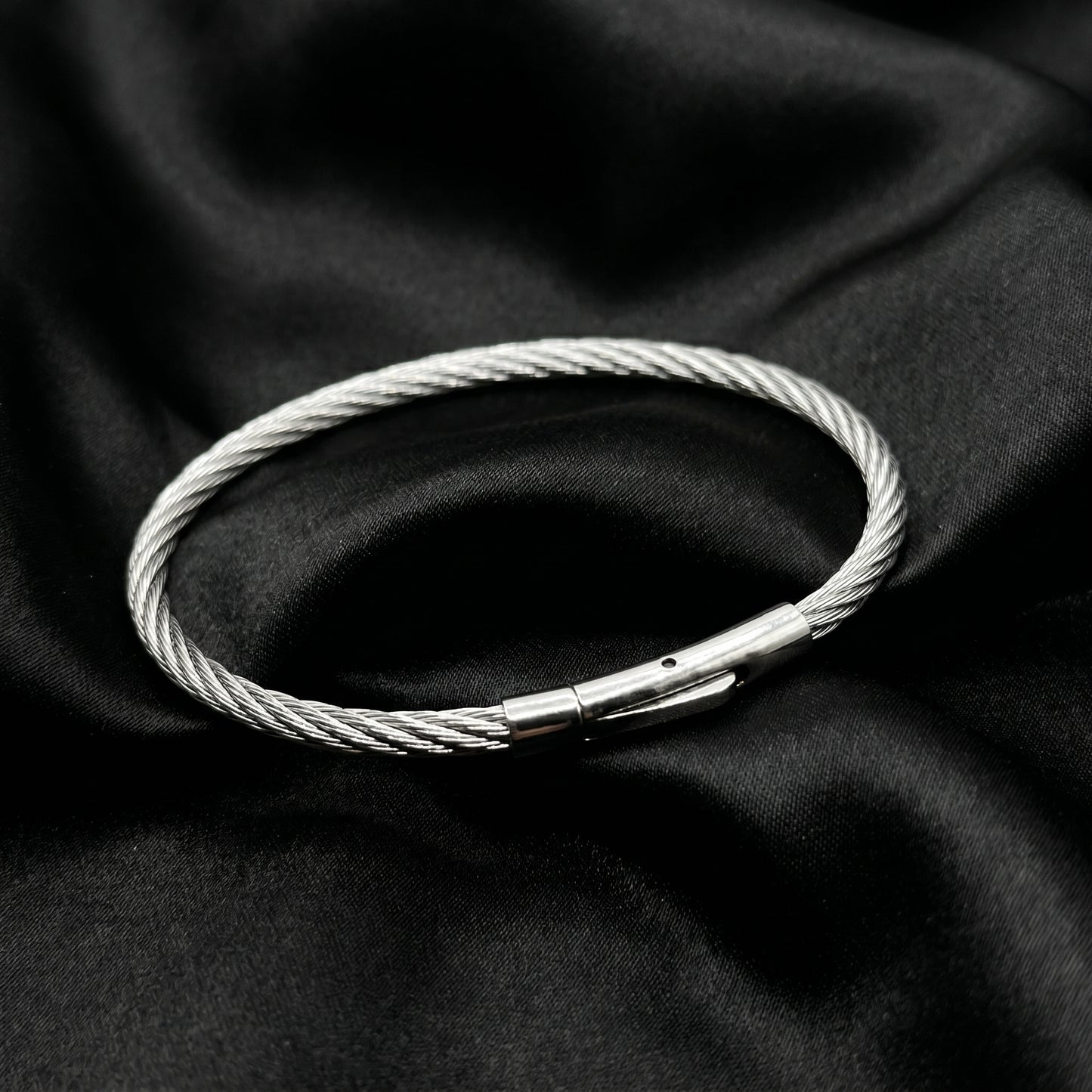 Silver stainless steel bracelet with a magnetic clasp, featuring a twisted wire design, set against a black fabric background