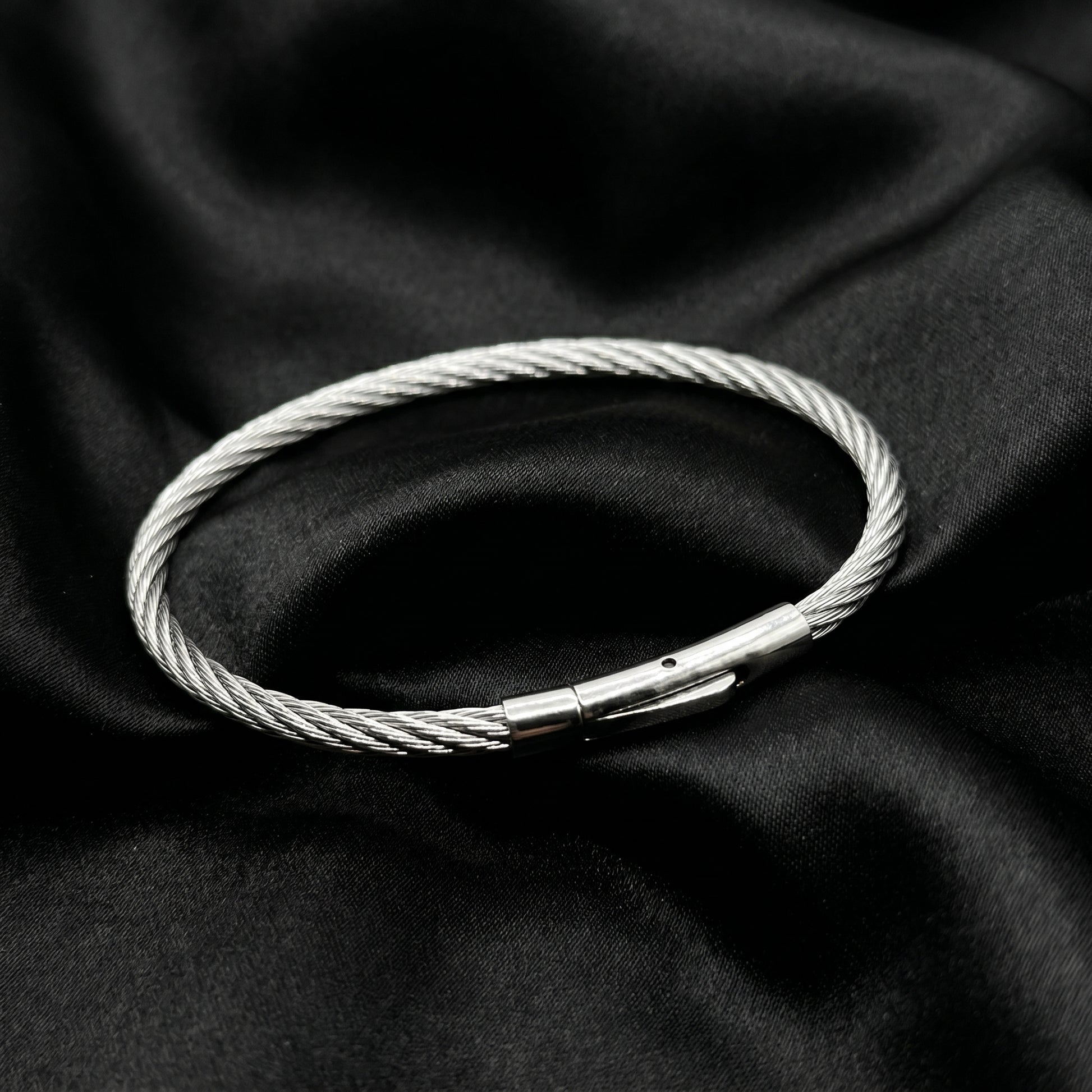 Silver stainless steel bracelet with a magnetic clasp, featuring a twisted wire design, set against a black fabric background