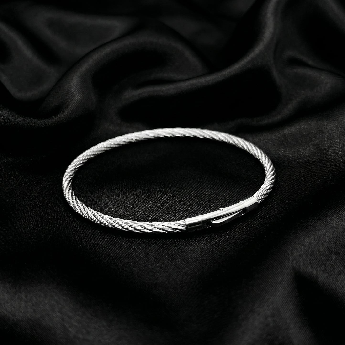 Silver stainless steel bracelet with a magnetic clasp, featuring a twisted cable design, displayed on a black satin backgroun