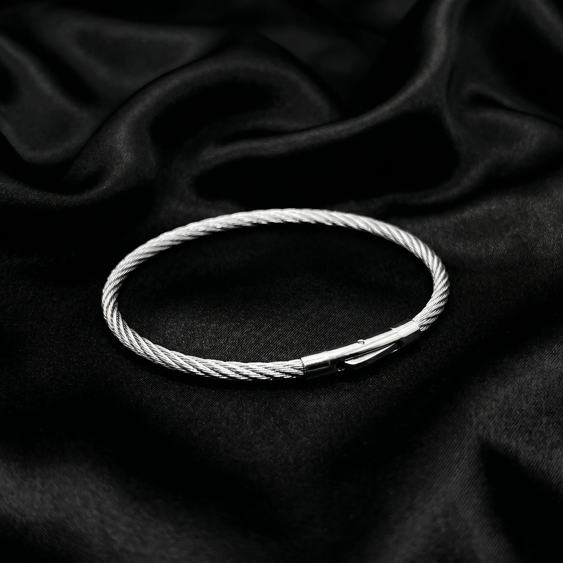 Silver stainless steel bracelet with a magnetic clasp, featuring a twisted cable design, displayed on a black satin backgroun